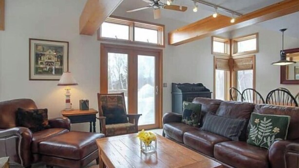 A living room with a brown leather sofa, a wooden coffee table with a vase of yellow flowers, a wooden chair, and a lamp. - 4 Season Spyglass Townhouse on Haystack Golf Course
Ski/Board/Golf/Hike/Relax (Wilmington)