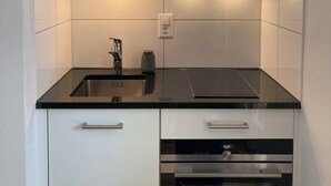 Eine moderne Küche mit weißen Schränken, einer schwarzen Arbeitsplatte, einer Edelstahl-Spüle und einem eingebauten Backofen.