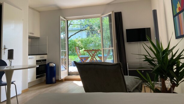 Ein modernes Wohnzimmer mit einer großen Schiebeglasdoor zum Balkon mit Blick auf Grünflächen.