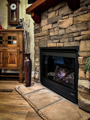 A stone fireplace with a modern TV screen, a wooden cabinet, and a decorative vase with branches.