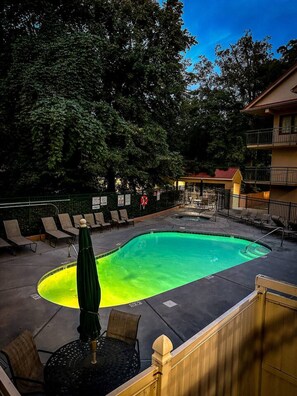 Una piscina con sillas de descanso y una sombrilla, rodeada de árboles y un edificio.