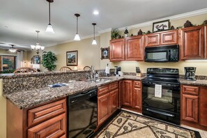 A kitchen with granite countertops, wooden cabinets, a black stove, and a microwave.