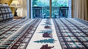A hotel room with a large bed, a view of a forest through a sliding glass door, and a balcony with a railing. - Downtown Gatlinburg Condo | Walk to Attractions! (Gatlinburg)