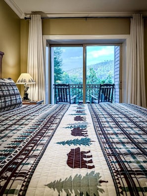 A hotel room with a large bed, a view of a forest through a sliding glass door, and a balcony with a railing. - Downtown Gatlinburg Condo | Walk to Attractions! (Gatlinburg)