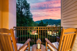 A balcony with two wooden chairs and a lantern, overlooking a residential area with houses and trees.
