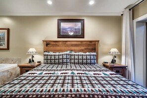 A bedroom with a wooden headboard, a patterned bedspread, two bedside lamps, and a framed picture on the wall.