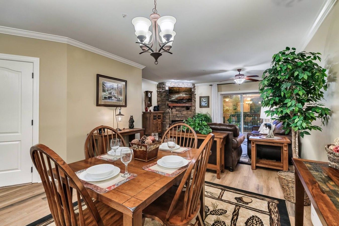 Un comedor con mesa de madera dispuesta para cuatro personas, rodeada de sillas, una araña y una chimenea de piedra.