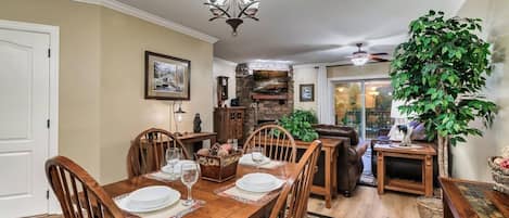 Un comedor con mesa de madera dispuesta para cuatro personas, rodeada de sillas, una araña y una chimenea de piedra.