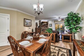 Un comedor con mesa de madera dispuesta para cuatro personas, rodeada de sillas, una araña y una chimenea de piedra.