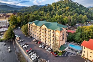 Um hotel com vários andares, teto verde, estacionamento e piscina.