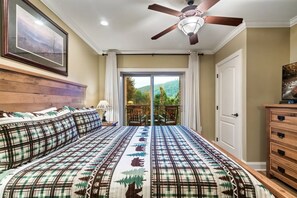 A bedroom with a bed, a ceiling fan, a door, and a view of a balcony.