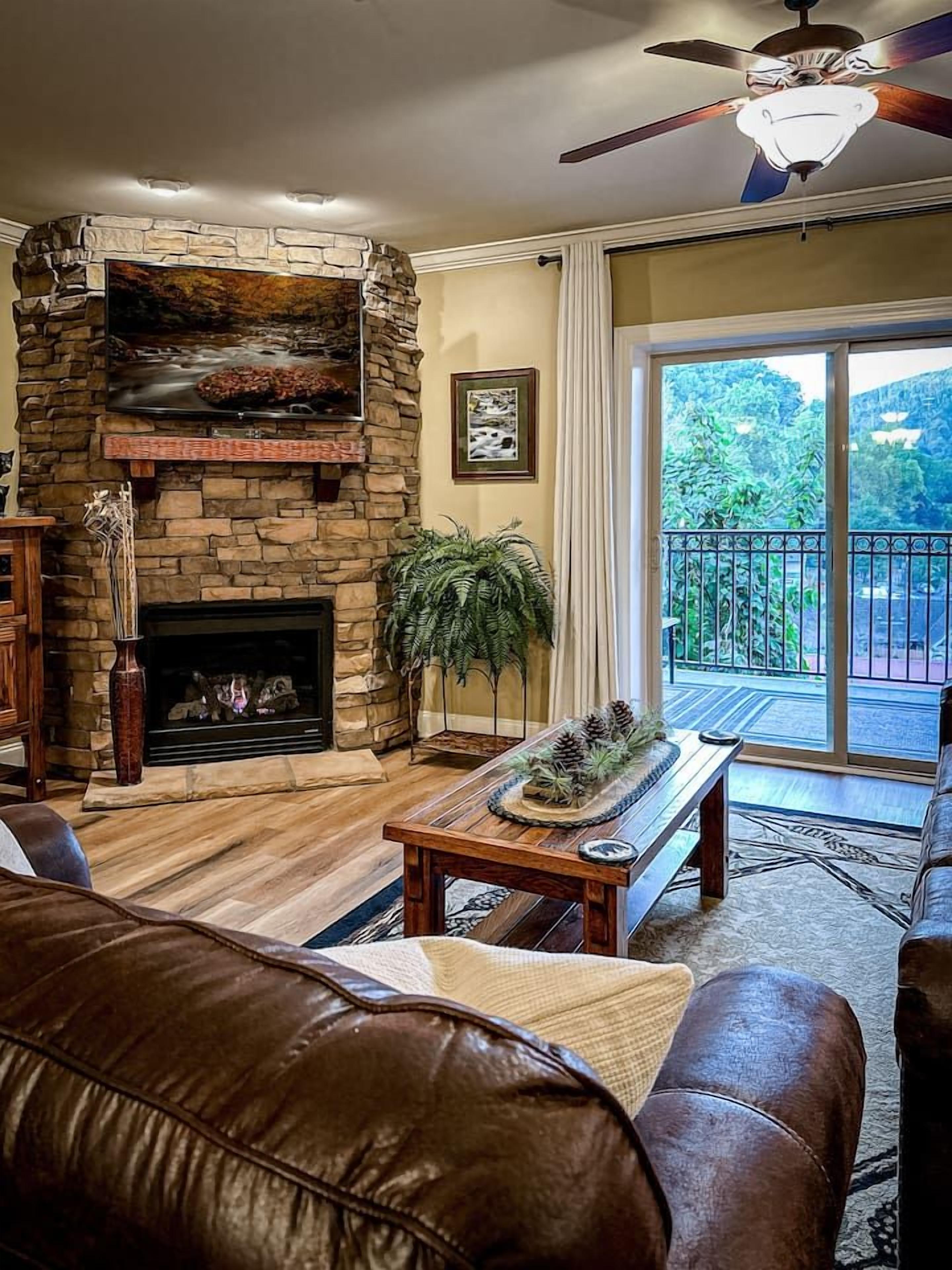 A living room with a stone fireplace, leather furniture, and a view of a balcony.