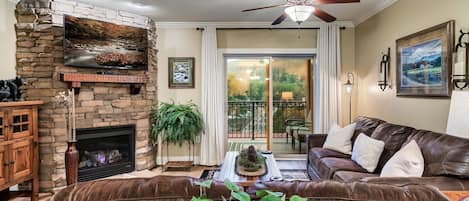 A living room with a stone fireplace, leather sofa, and a ceiling fan.