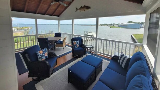 A covered outdoor seating area with a view of the water, featuring a table and chairs, a sofa, and a ceiling fan. - High Water Guest House<br> (Cambridge)
