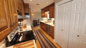 A modern kitchen with wooden cabinets, a stainless steel stove, and a white door. - High Water Guest House<br> (Cambridge)