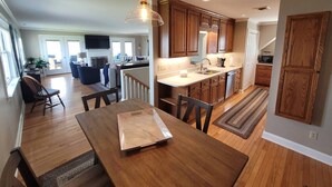 A modern kitchen with wooden cabinets, a dining area with a wooden table, and a living room with a fireplace. - High Water Guest House<br> (Cambridge)