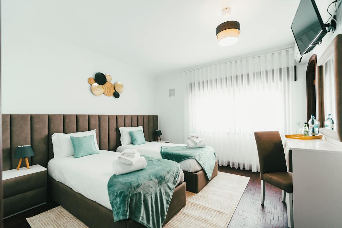 A hotel room with two beds, a desk, a chair, a TV, and a large window with curtains.