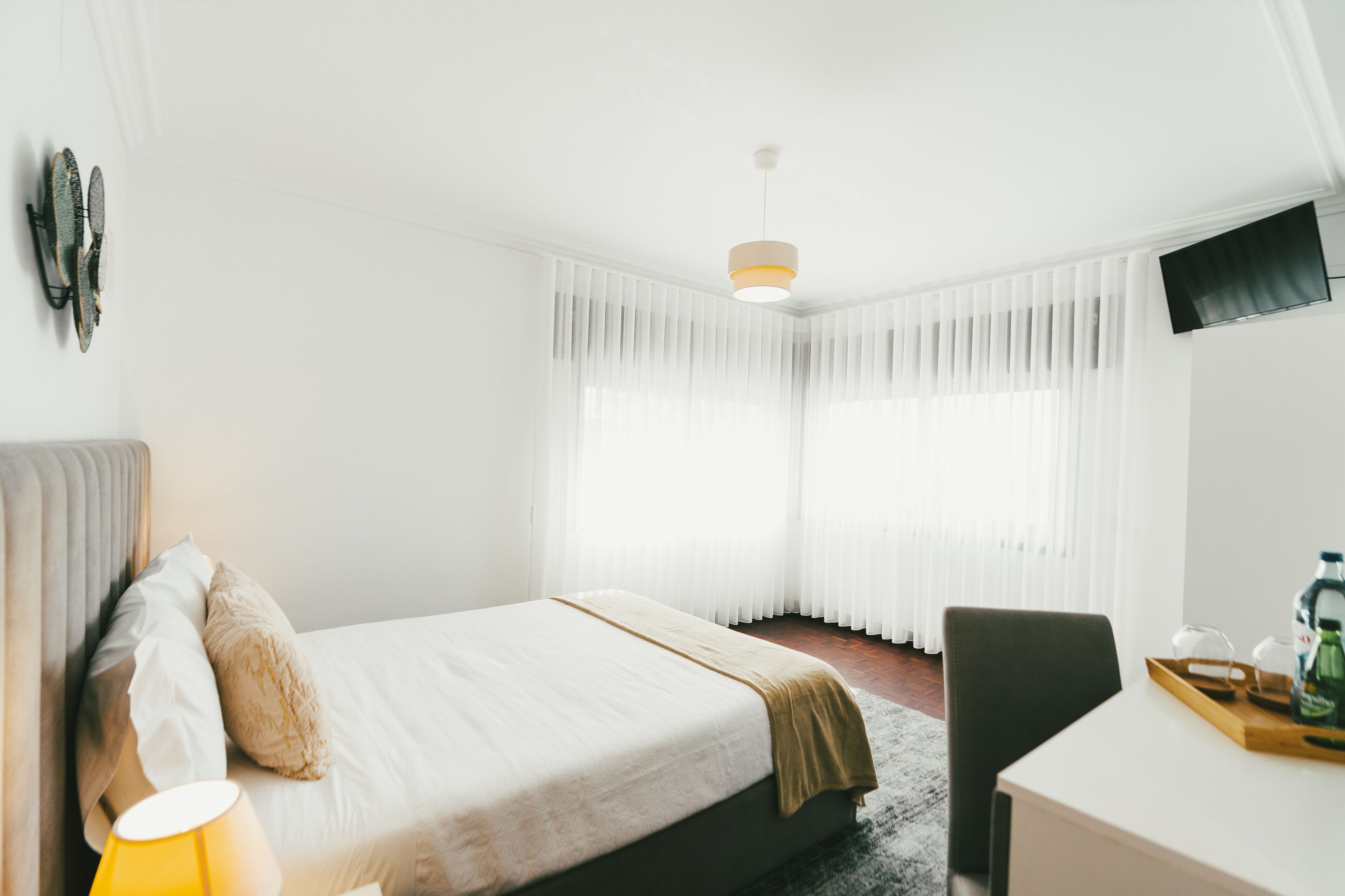 A hotel room with a bed, a desk, a chair, a lamp, and a TV on the wall.