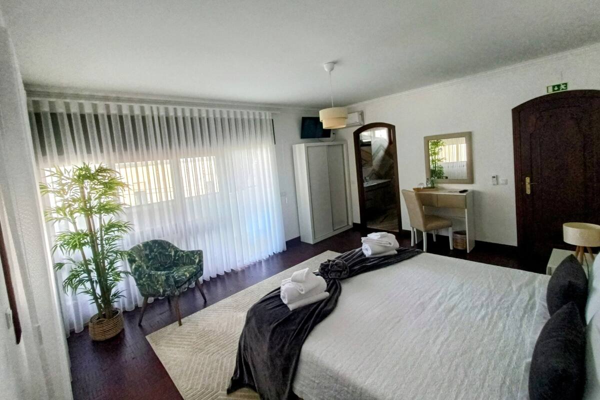 A hotel room with a bed, a desk, a chair, a mirror, and a potted plant.