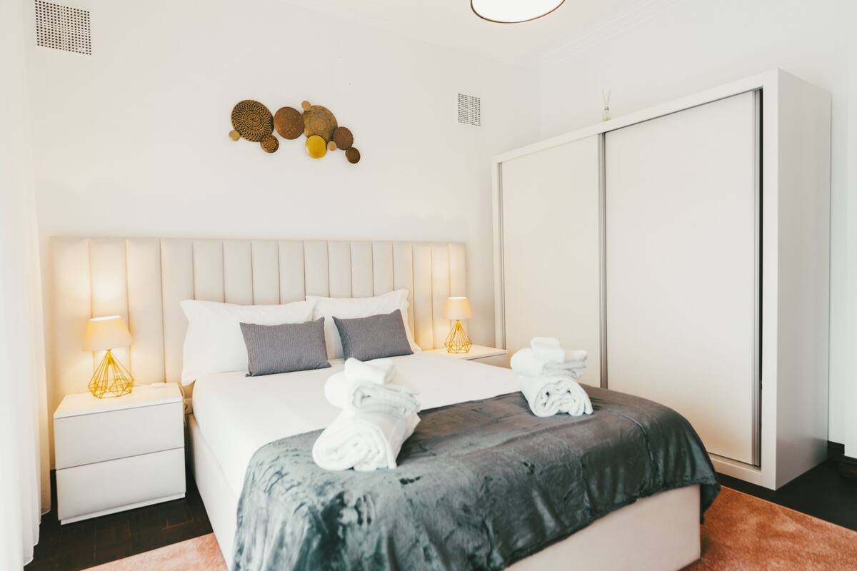 A modern hotel room with a large bed, two bedside tables with lamps, a wardrobe, and decorative wall art.