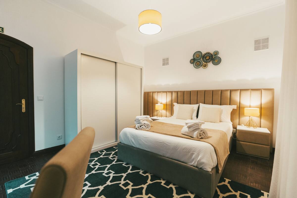 A hotel room with a bed, bedside lamps, a nightstand, a wardrobe, and a patterned rug.