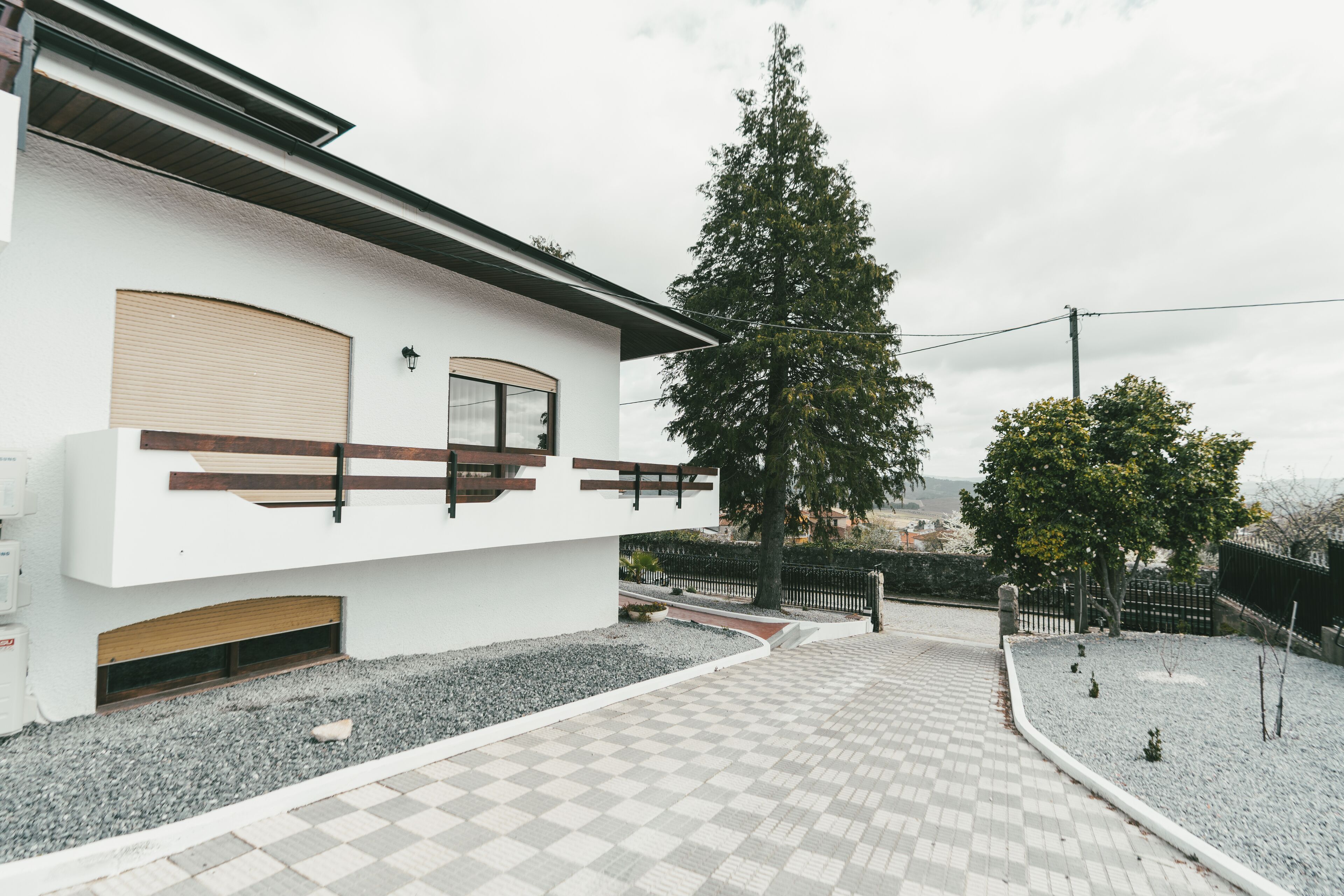 A modern building with a white facade, a wooden deck, and a large tree in the background.