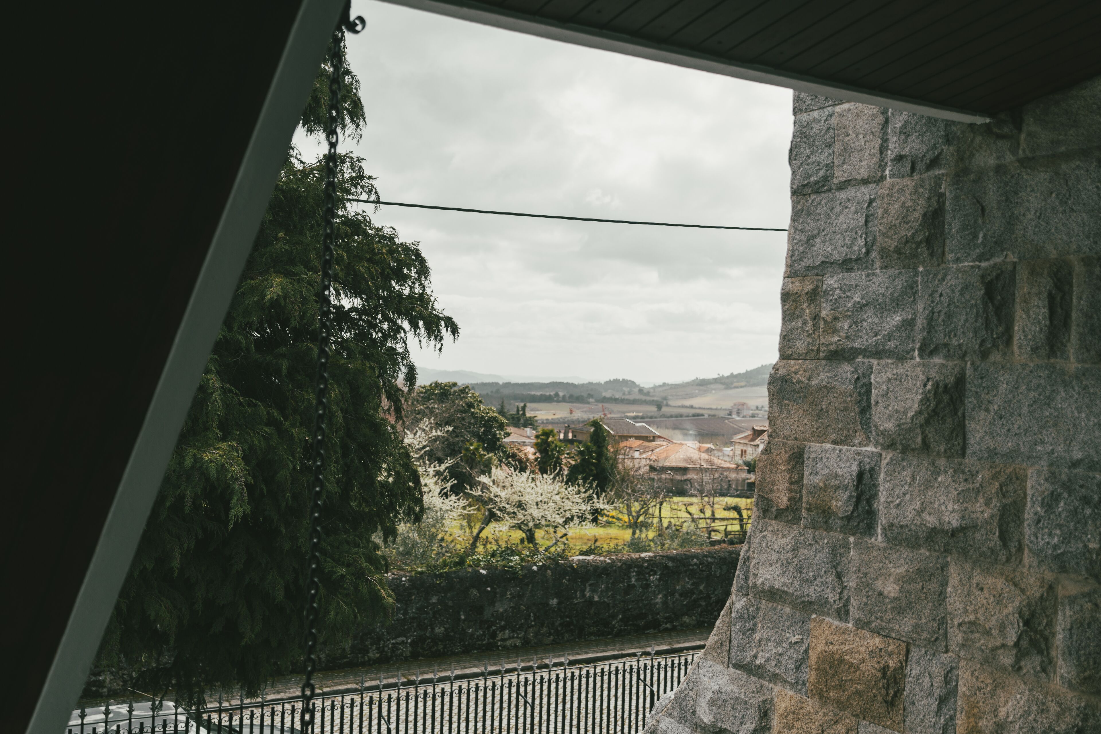 A view from a window overlooking a stone wall and a garden with trees and a fence.