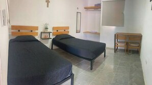 A room with two single beds, a small table, a chair, a shelf with books, and a cross on the wall. - Elegant Blue 6 min From Airport ! (Mérida)