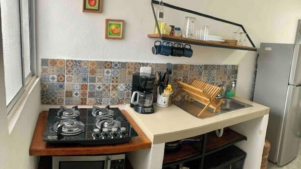A compact kitchen with a gas stove, microwave, and a sink with a wooden drying rack. - Elegant Blue 6 min From Airport ! (Mérida)