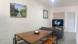 A living room with a wooden dining table, grey sofa, and a television on a stand. - Elegant Blue 6 min From Airport ! (Mérida)