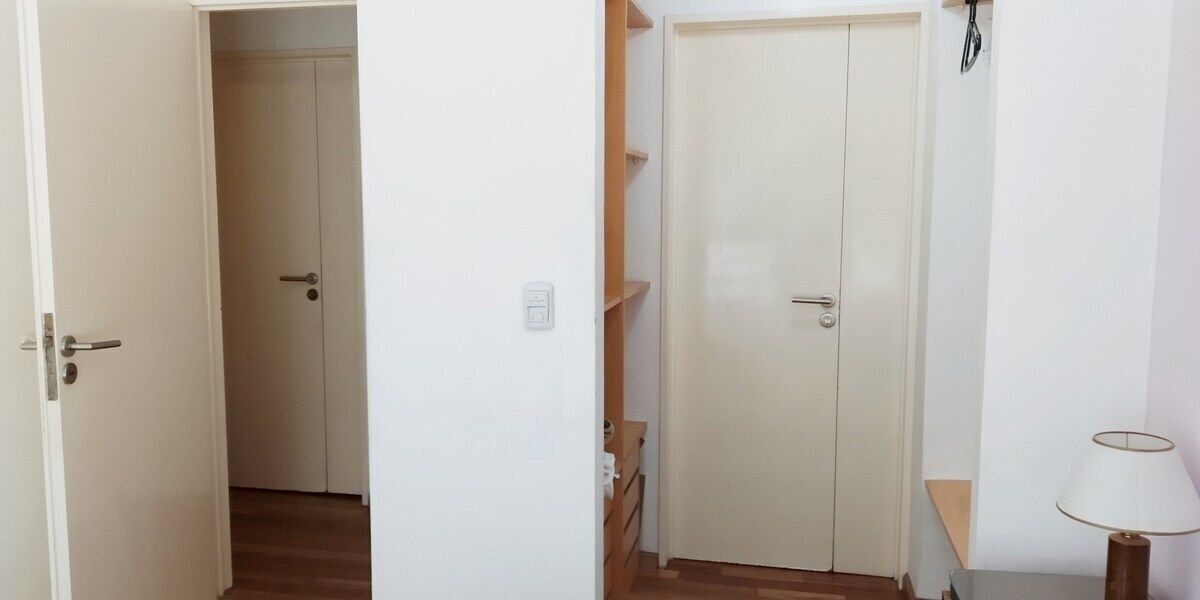 A hallway with a closed door, a small table with a lamp, and a wooden floor.