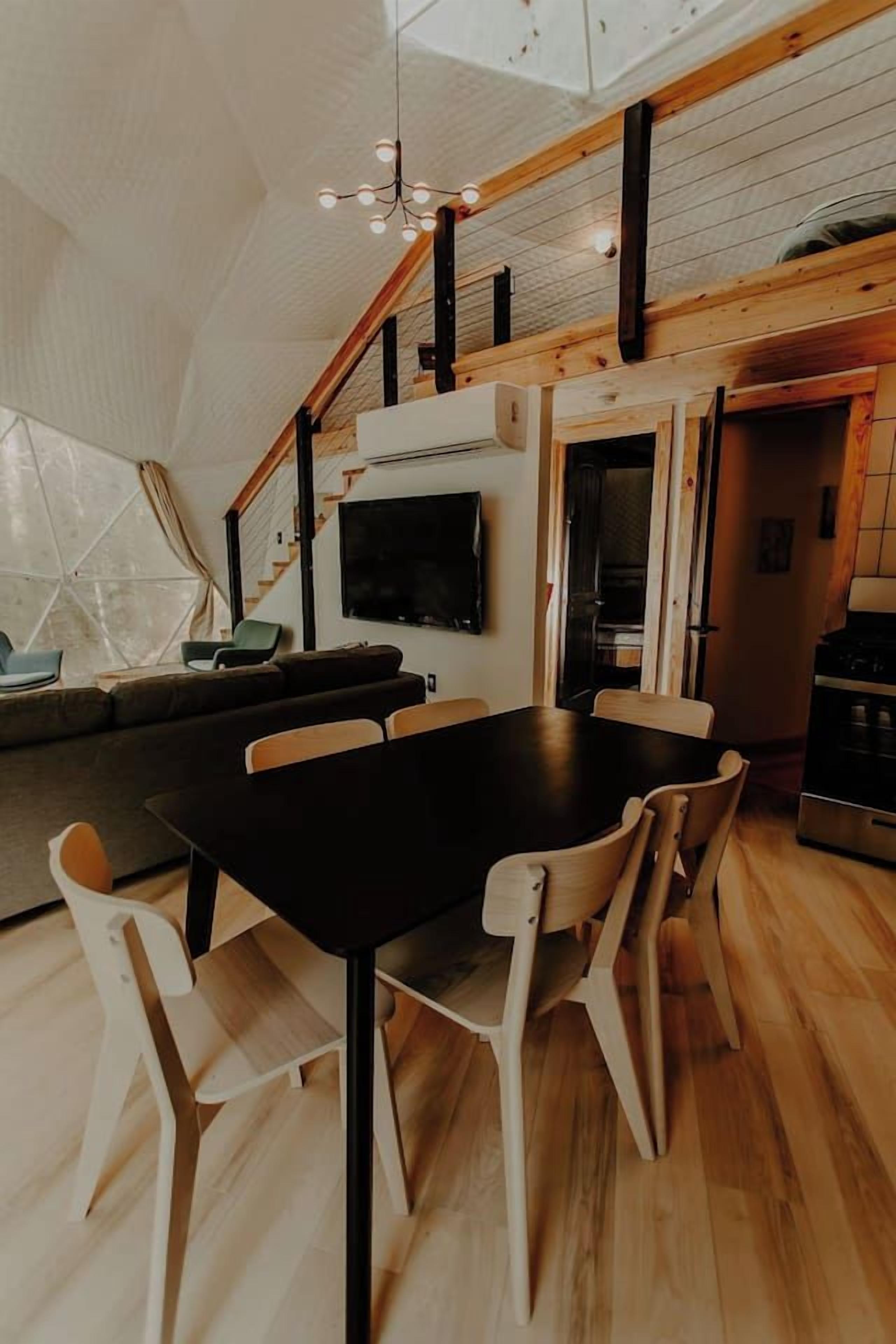 A modern kitchen with a black dining table and chairs, a built-in oven, and a television mounted on the wall.