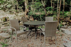 Un espace extérieur aménagé avec une table ronde et quatre chaises, entouré de végétation naturelle et de rochers.