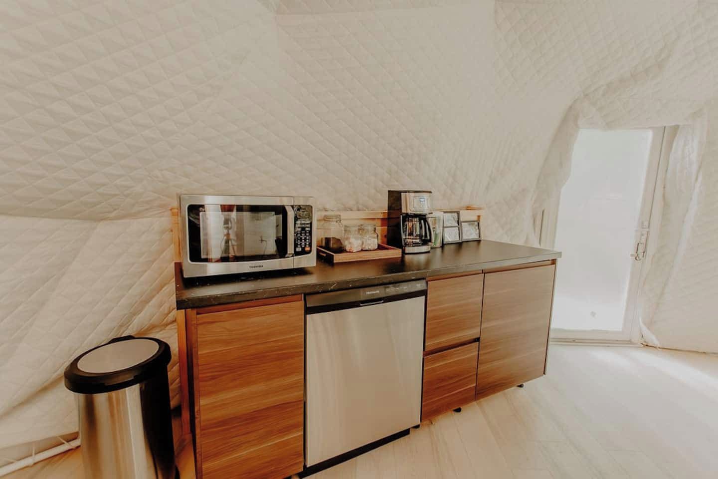 Un angolo cottura compatto completo di forno a microonde, macchina del caffè e piccolo frigorifero.