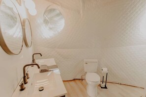 Un baño pequeño y de diseño blanco, con inodoro, lavabo y dos espejos.