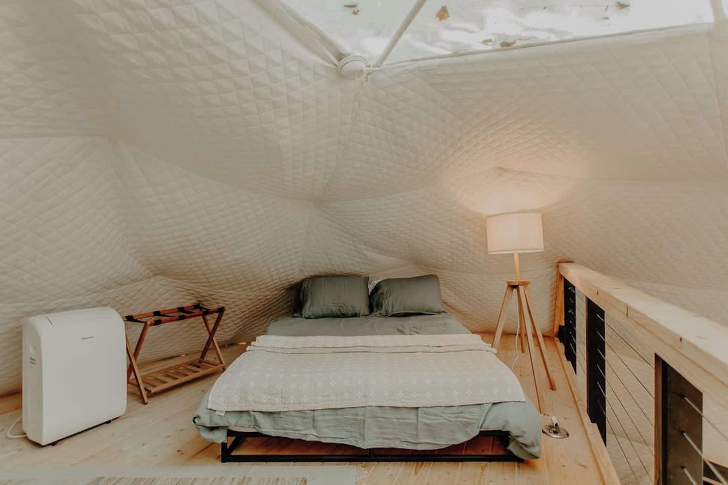 A compact, triangular room with a bed, a standing lamp, and a small white appliance.