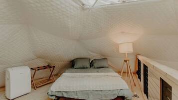 A compact, triangular room with a bed, a standing lamp, and a small white appliance.