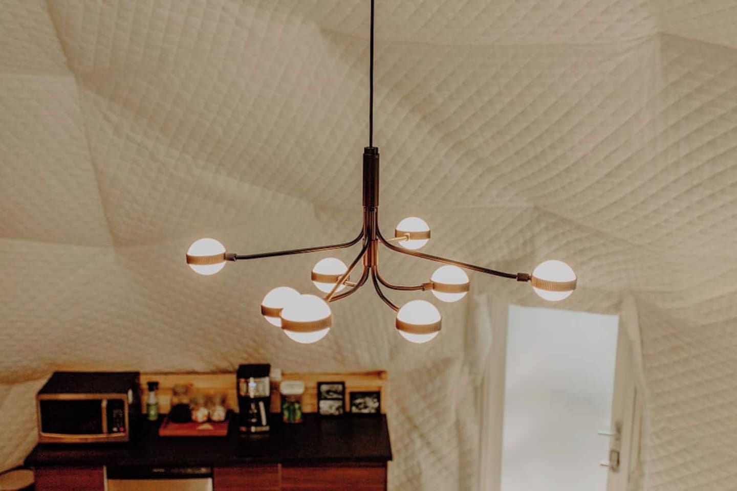 A modern interior with a unique textured ceiling and a central chandelier with multiple spherical lights.