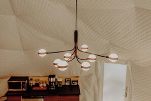 Un intérieur moderne, doté d’un plafond à la texture originale et d’un lustre central composé de plusieurs sphères lumineuses.