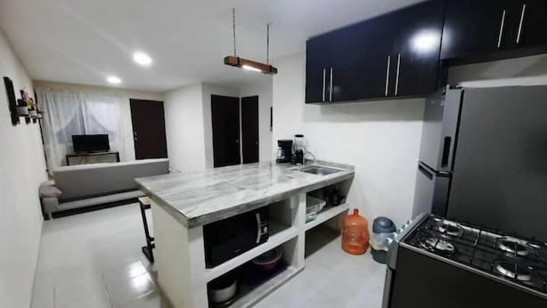 Une cuisine de taille réduite avec un îlot central, des meubles de couleur sombre, un réfrigérateur et une cuisinière à gaz.