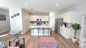A modern kitchen with white cabinets, a central island with bar stools, and a refrigerator.