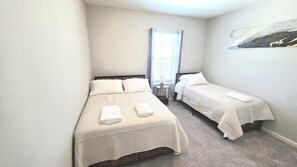 A small, clean room with two single beds, a small table, and a window with curtains.