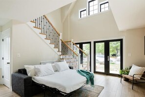 A bedroom with a bed, a staircase, and a view through large windows. - Private Sunny Cottage with King Bed + Yard / Patio (Arlington)