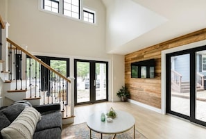 A spacious living room with a staircase, large windows, and a wooden accent wall. - Private Sunny Cottage with King Bed + Yard / Patio (Arlington)