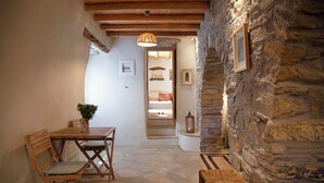 A cozy dining area with a stone wall, wooden furniture, and a hanging light fixture. - Under the Linden Tree Tinos (Tinos)
