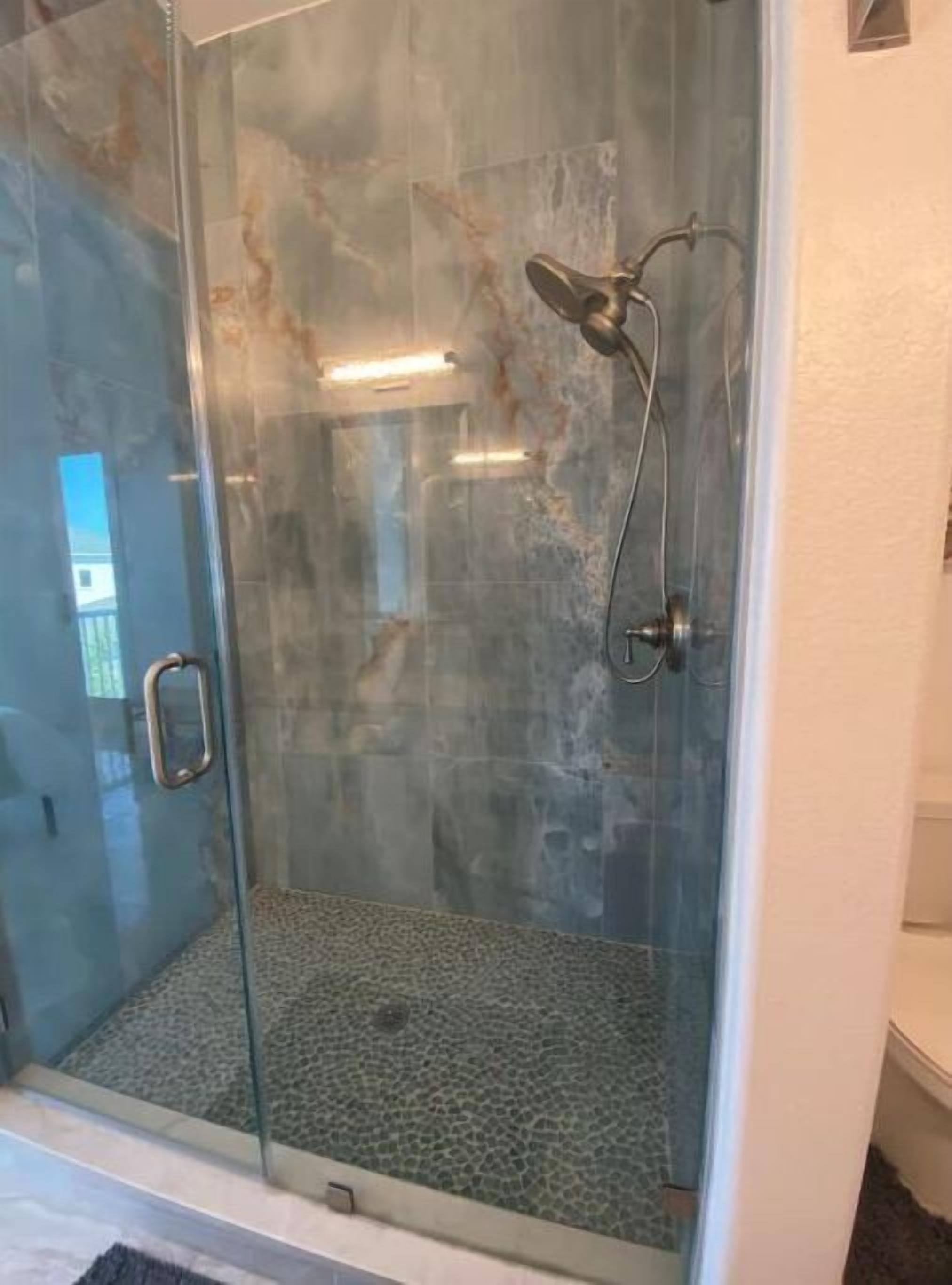 A glass-enclosed shower with a textured floor, a handheld showerhead, and a wall-mounted control panel.