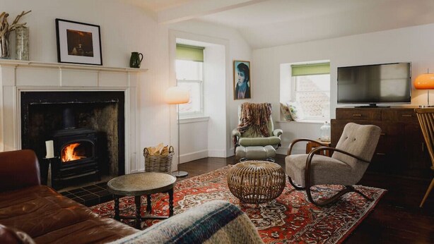 A cozy living room with a fireplace, comfortable seating, a television, and a large window. - TCN · The Crow's Nest, Pittenweem - Your Seaside Retreat (Pittenweem, Fife,)