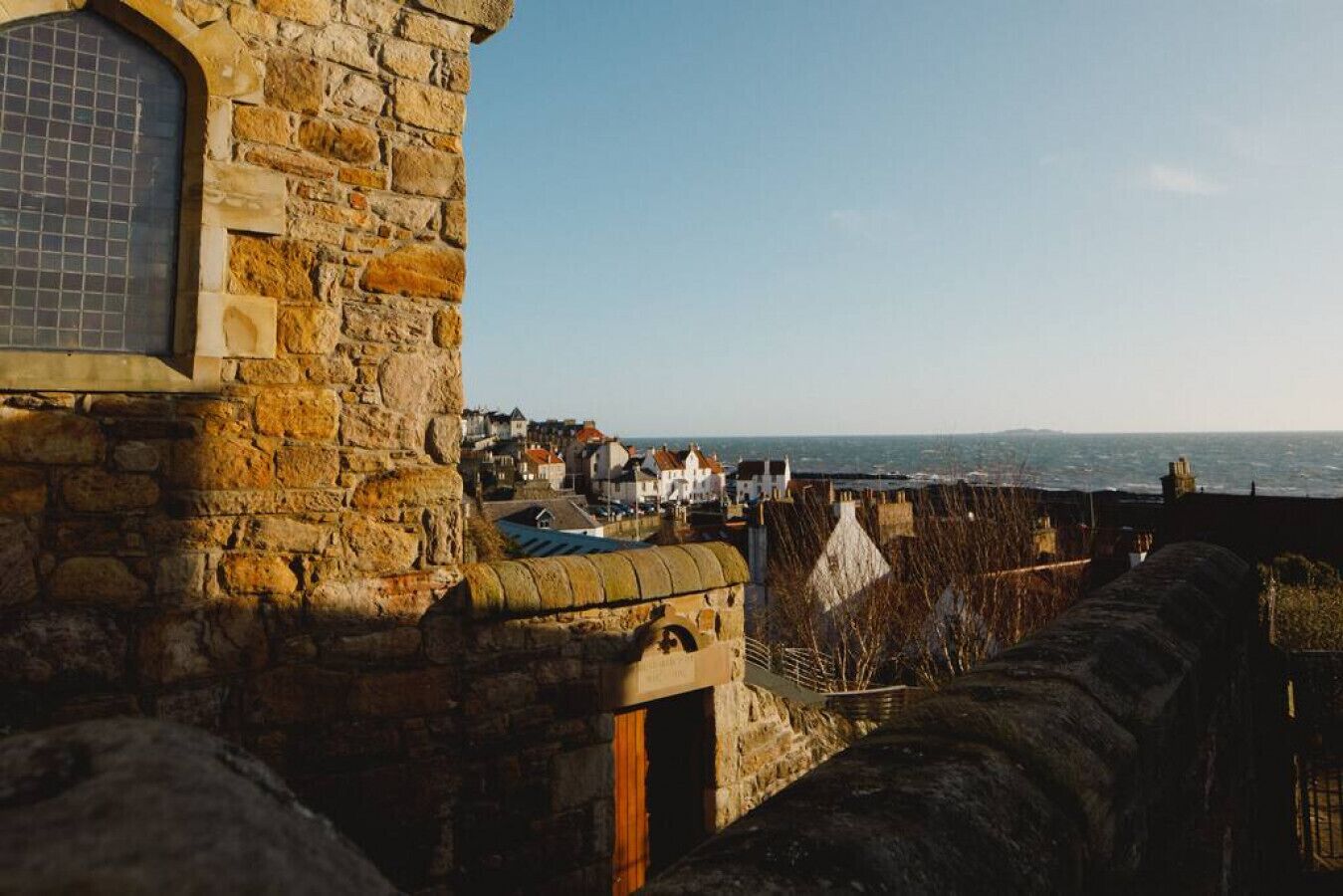 A stone building with a window and a view of a coastal town.