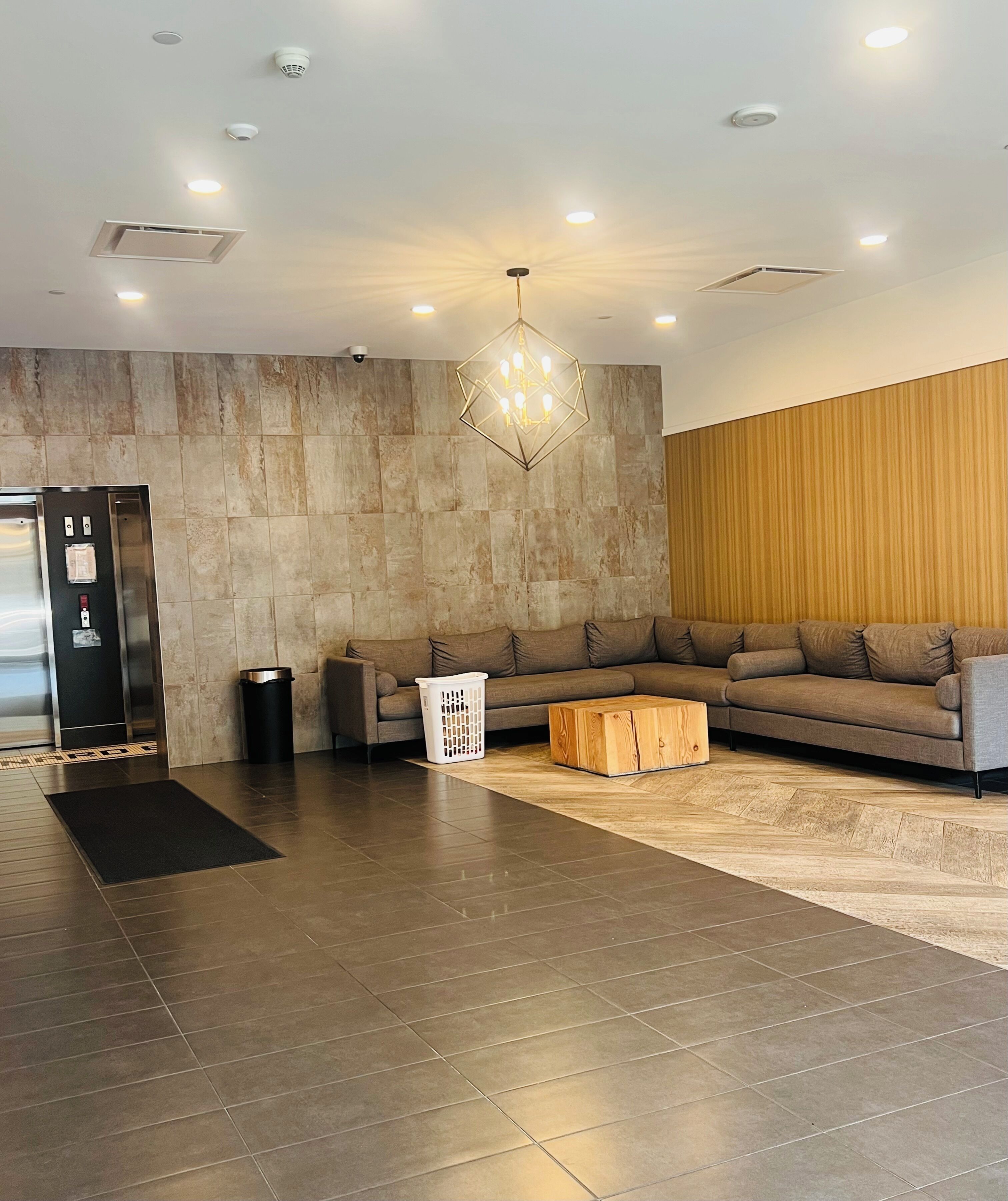 Um lobby moderno com parede de pedra, painel de madeira, sofá cinza, mesa de centro de madeira e lixeira.