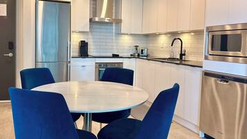 Una cocina moderna con gabinetes blancos, electrodomésticos de acero inoxidable y una mesa redonda con sillas azules.